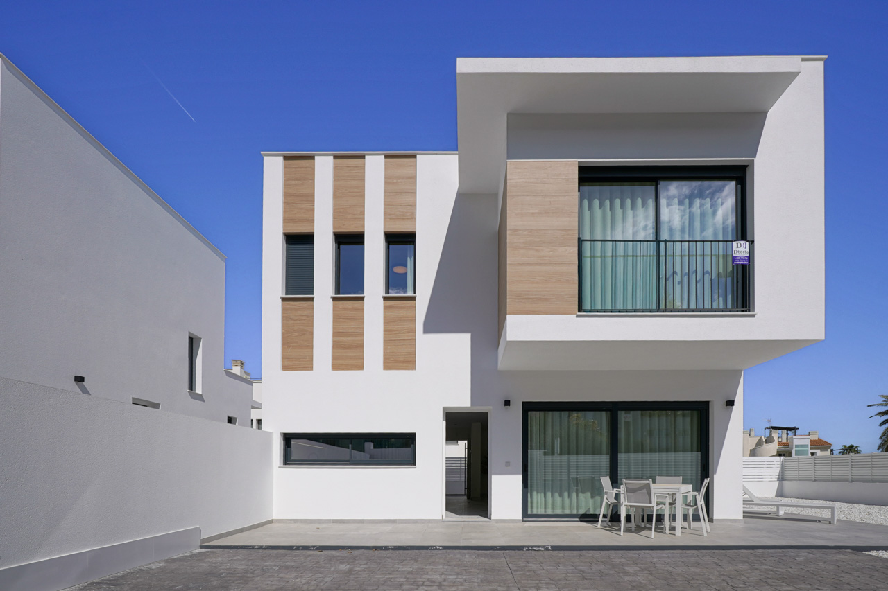 Moderne gevel van de villa met witte afwerking, houtlook accenten, een ruim terras op de begane grond en een uitstekende bovenverdieping met balkon.