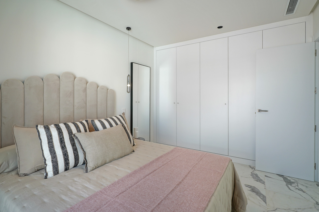 Moderne slaapkamer met kamerhoge witte inbouwkasten, een geaderde marmeren vloer en een gestoffeerd hoofdbord met boogontwerp en hangverlichting.