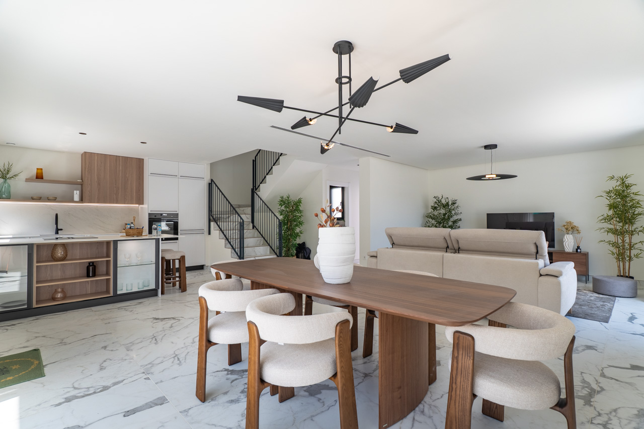 Open leefruimte met een houten eettafel, een moderne keuken met marmerlook afwerking en een strakke trap met zwart metalen leuning.