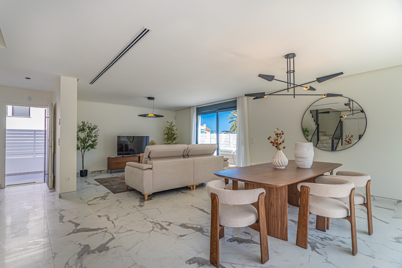 Open woon- en eetkamer met een marmerlook porseleinen vloer, modern houten meubilair en grote glazen schuifdeuren naar het terras.