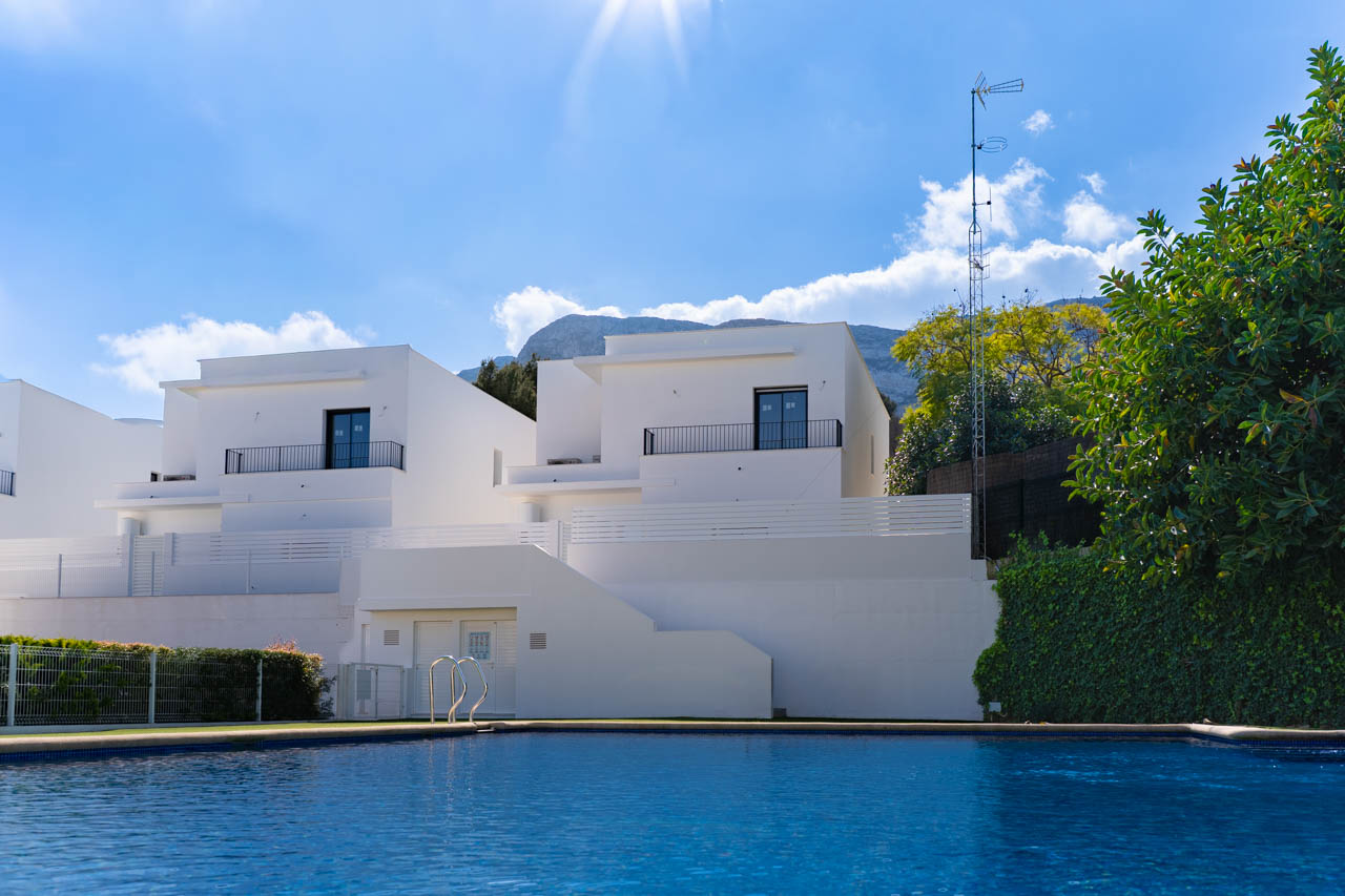 Zicht op de moderne villa's vanaf het gemeenschappelijke zwembad, met witte minimalistische gevels en het Montgó-gebergte op de achtergrond.
