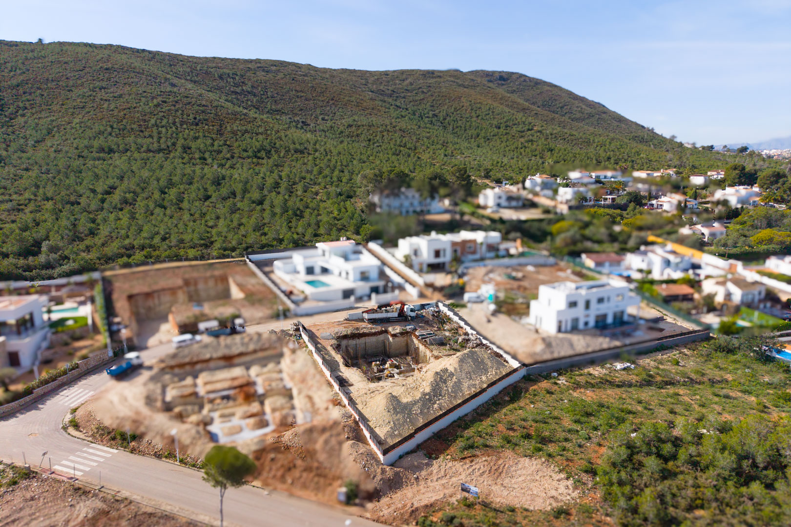 Luchtfoto van het bouwperceel in Valsol, met de eerste fase van uitgraving en fundering te midden van moderne villa's en de groene heuvels van Jávea.