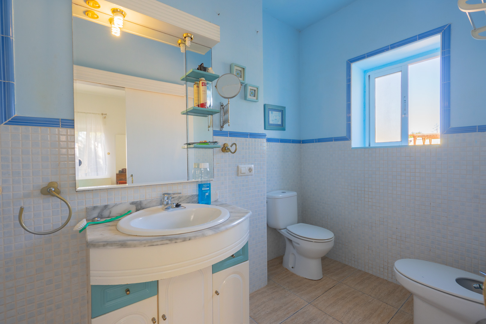Badkamer met blauw-witte mozaïektegels, een wastafelmeubel met marmeren blad en natuurlijk lichtinval via een zijraam.