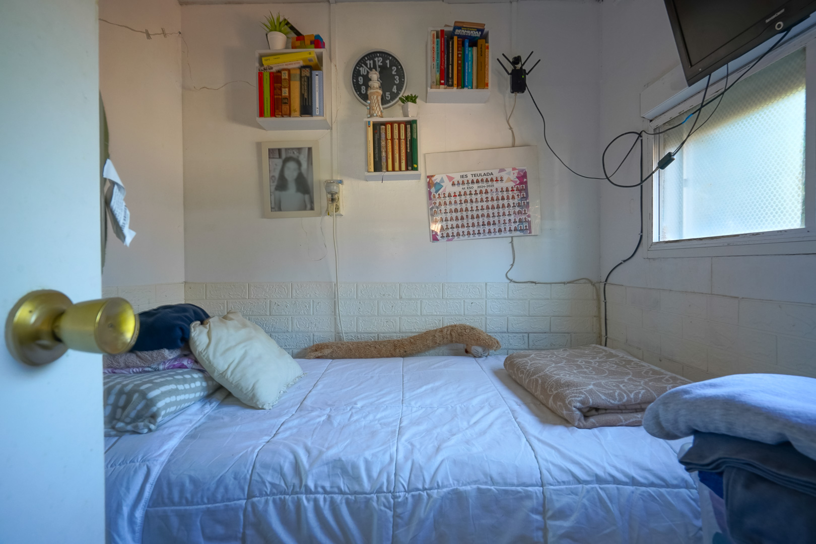 Compacte slaapkamer met eenpersoonsbed, wandplanken en zijraam. De wanden zijn afgewerkt met een witte lambrisering met baksteenmotief.