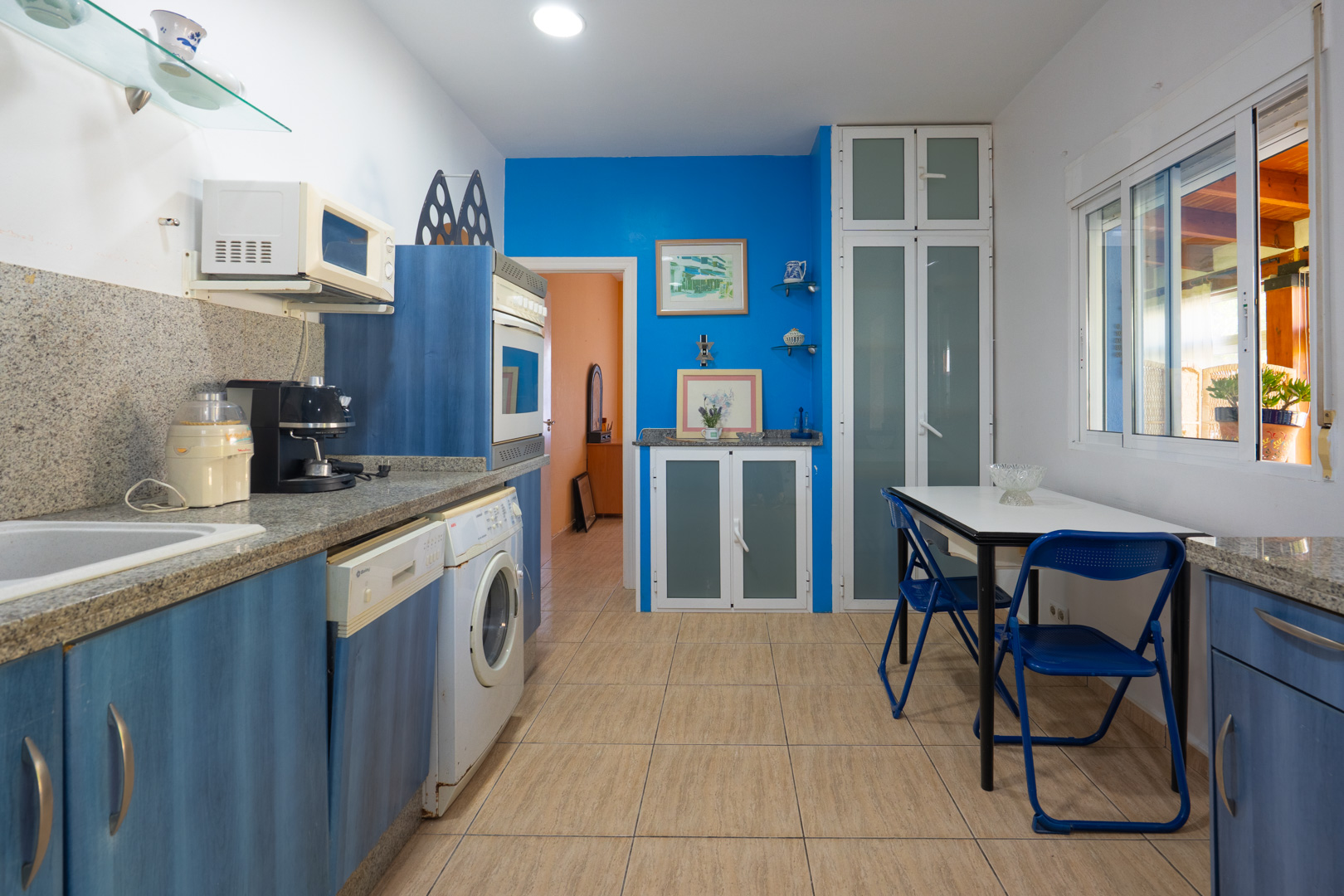 Ingerichte keuken met blauwe kasten, grijs granieten werkbladen, een ontbijthoek en geïntegreerde apparatuur onder inbouwverlichting.
