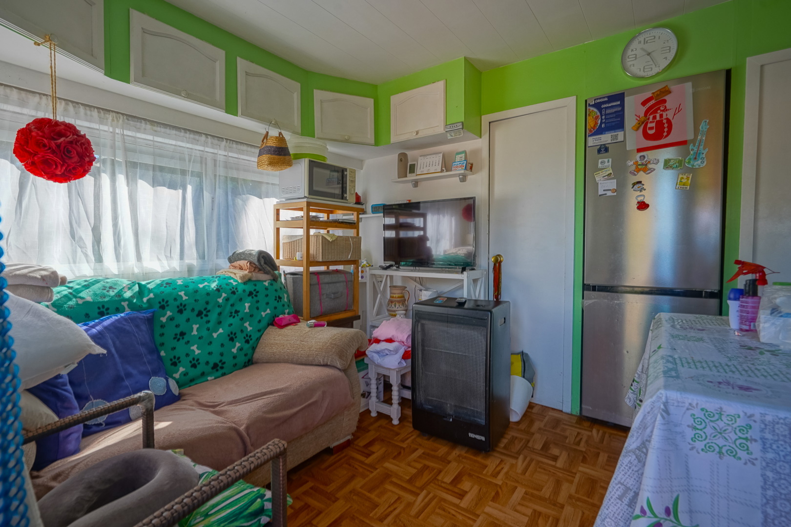 Interieur van het prefab bijgebouw met groene muren, compacte zithoek, parketvloer en open keuken voorzien van roestvrijstalen apparatuur.