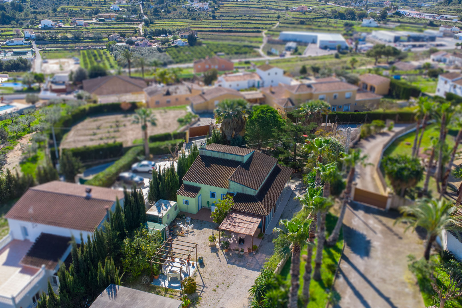 Luchtfoto van de traditionele finca met groene gevel, pannendak en buitenruimtes met houten pergola's en palmbomen op een ruim perceel.