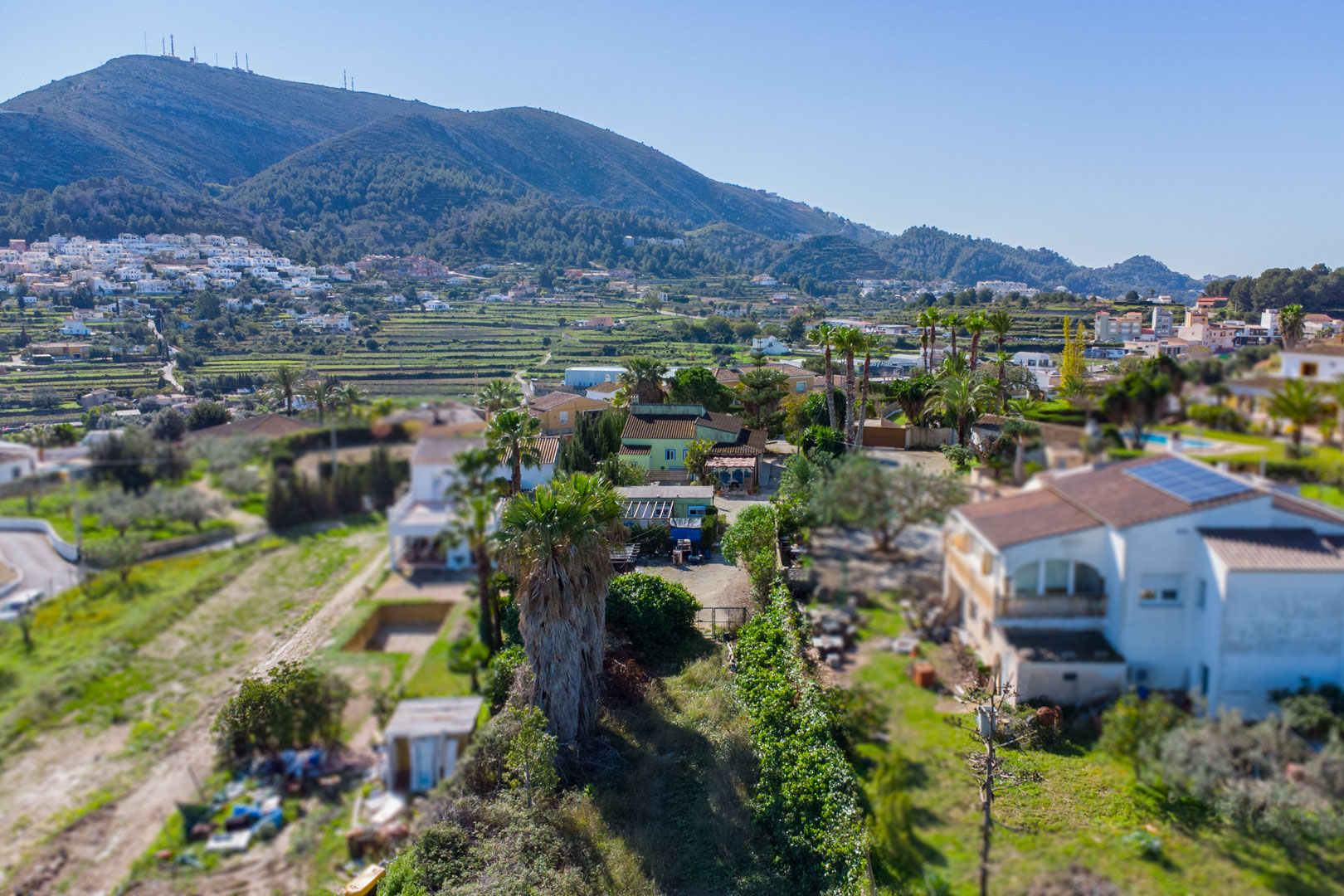 Luchtfoto van het rustieke perceel met de groene hoofdwoning, de prefab unit en het omliggende terrassenlandschap met uitzicht op de bergen.