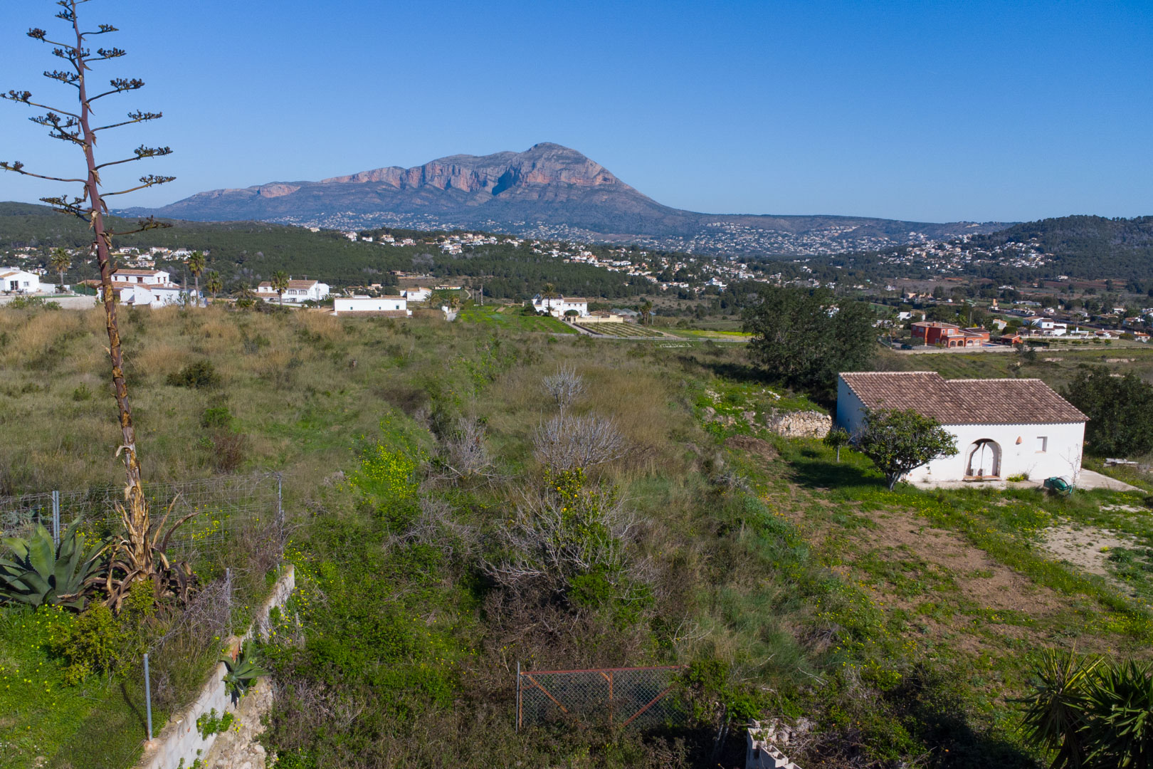 Panoramisch uitzicht vanaf het rustieke perceel over de vallei van Benitachell, met de berg Montgó op de achtergrond en natuurlijke begroeiing.