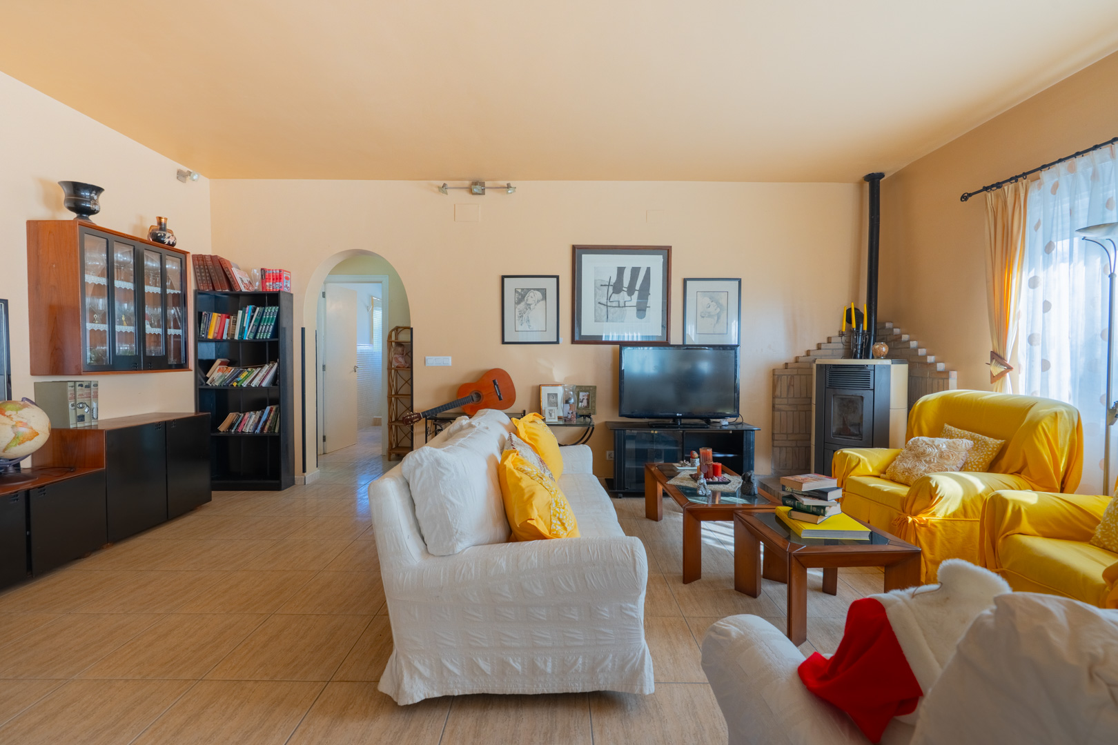 Ruime woonkamer in traditionele stijl met houtkachel, keramische tegelvloer en een karakteristieke boogdoorgang naar de rest van de woning.