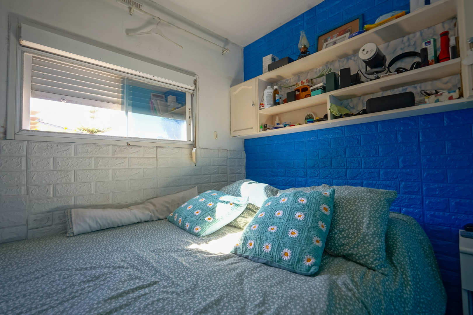 Slaapkamer in de prefabwoning met blauwe en witte muren in baksteenlook, geïntegreerde planken en natuurlijk licht.