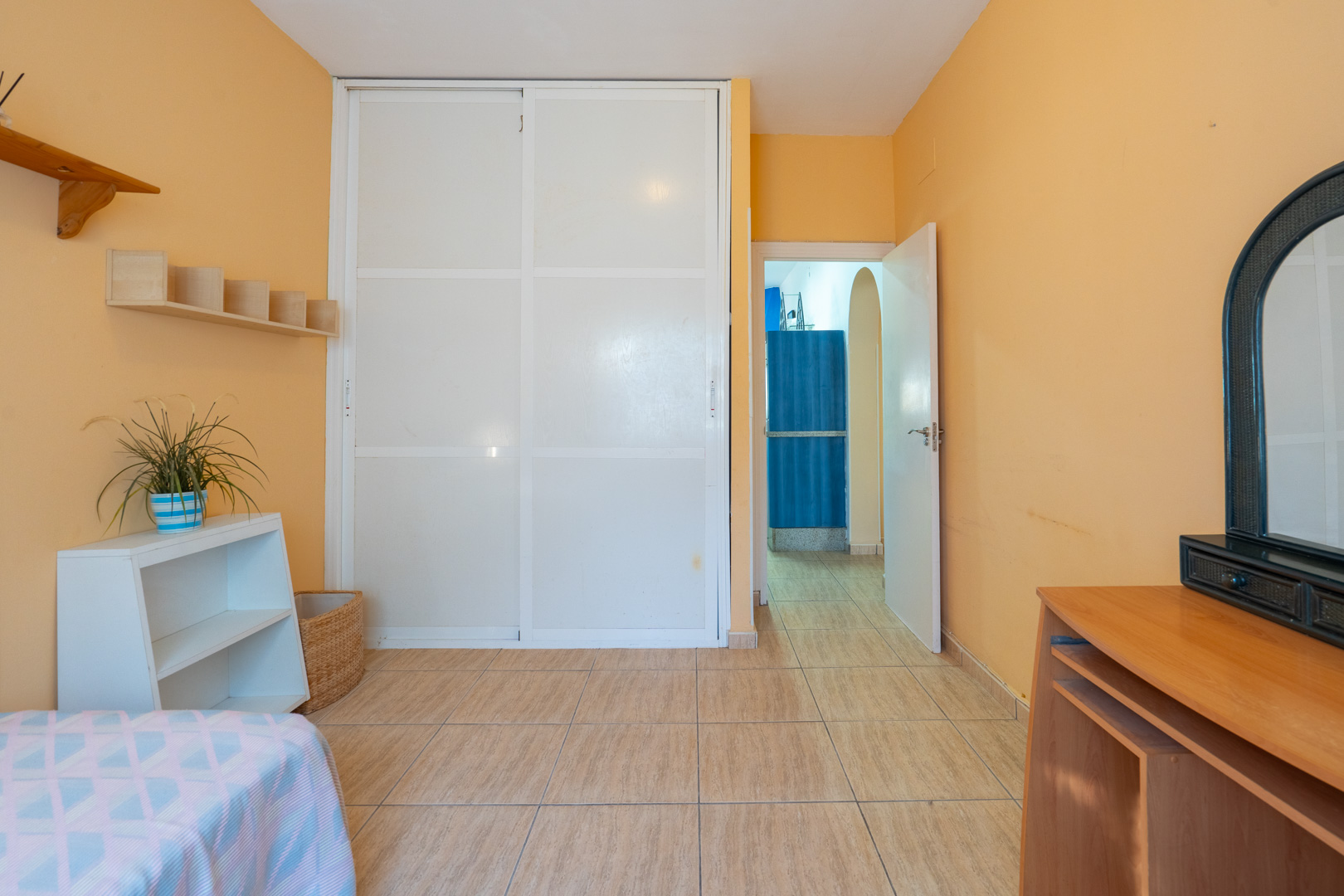 Slaapkamer met perzikkleurige wanden, een witte inbouwkast met schuifdeuren, keramische tegelvloer en doorgang naar de hal.