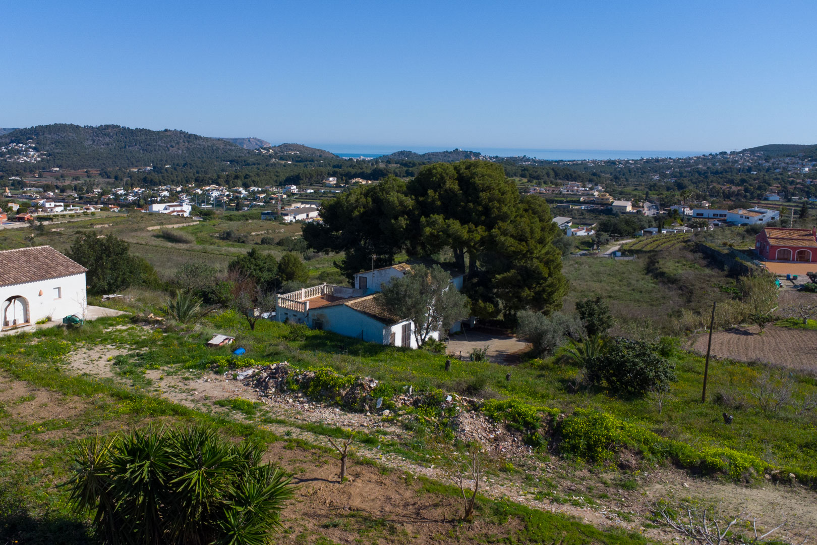 Verhoogd zicht op de traditionele finca en het rustieke perceel, met panoramisch uitzicht over de vallei van Benitachell tot aan de Middellandse Zee.