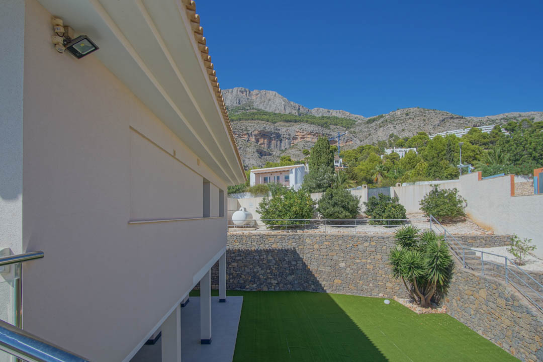 Buitenaanzicht van de lagergelegen tuin met kunstgras, natuurstenen muren en metalen trappen tegen de achtergrond van de Sierra de Altea.