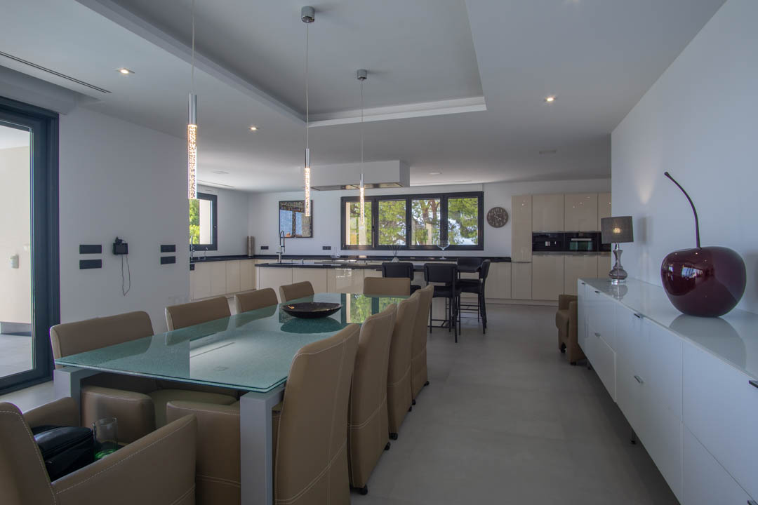 Design eethoek met glazen tafel en lederen stoelen, geïntegreerd in een open keuken met donkere werkbladen en inbouwverlichting.