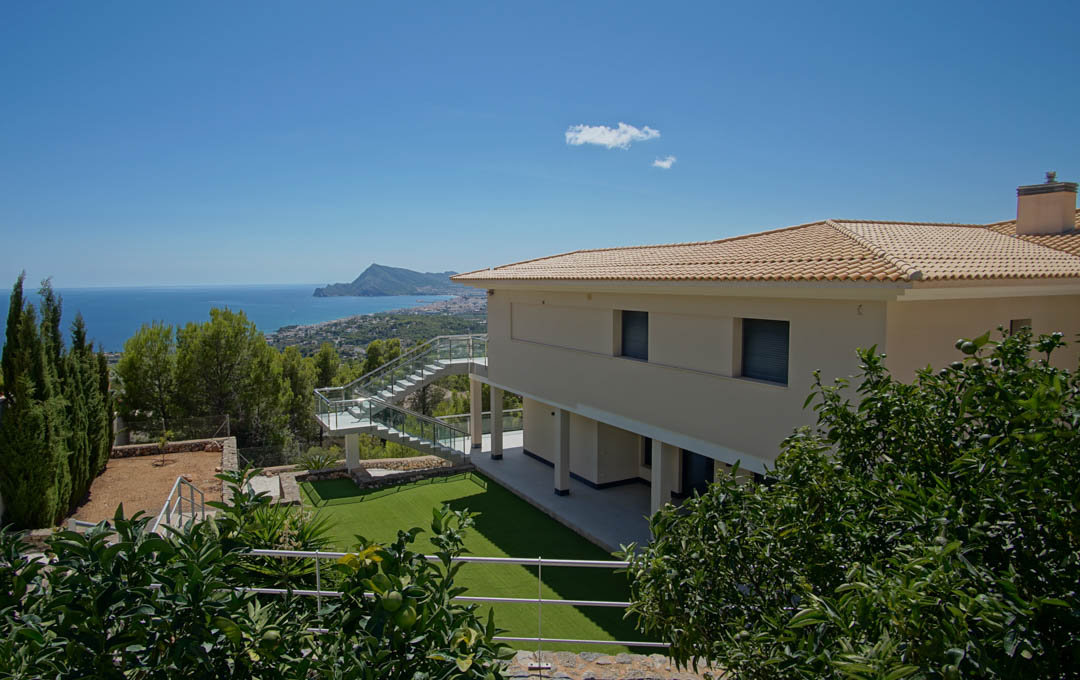 Exterieur van de villa met kunstgrasveld, fruitbomen en glazen trap, uitkijkend over de baai van Altea en de Middellandse Zee.