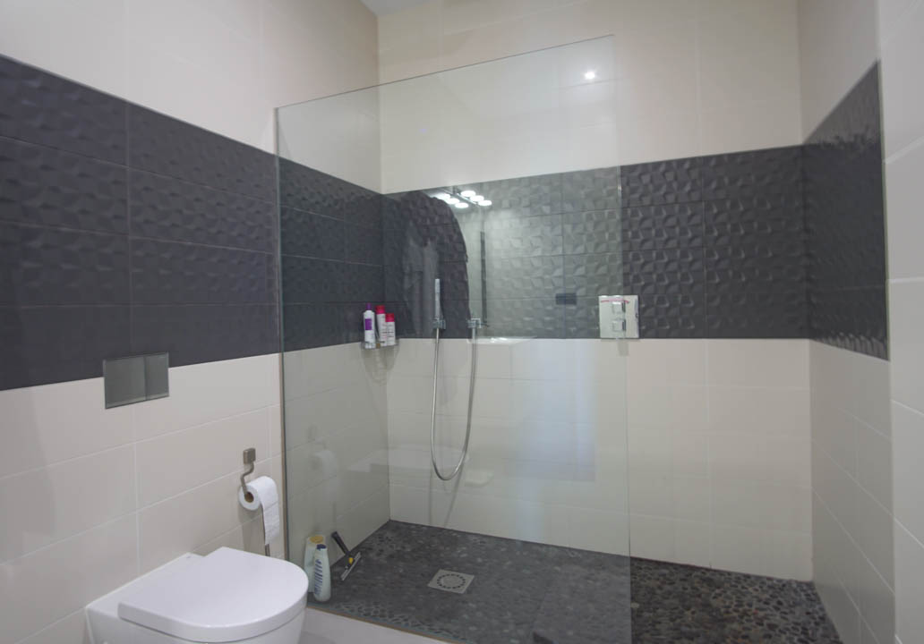 Moderne badkamer met inloopdouche, glazen wand, kiezelvloer en contrasterende wandtegels met een geometrisch reliëfpatroon.