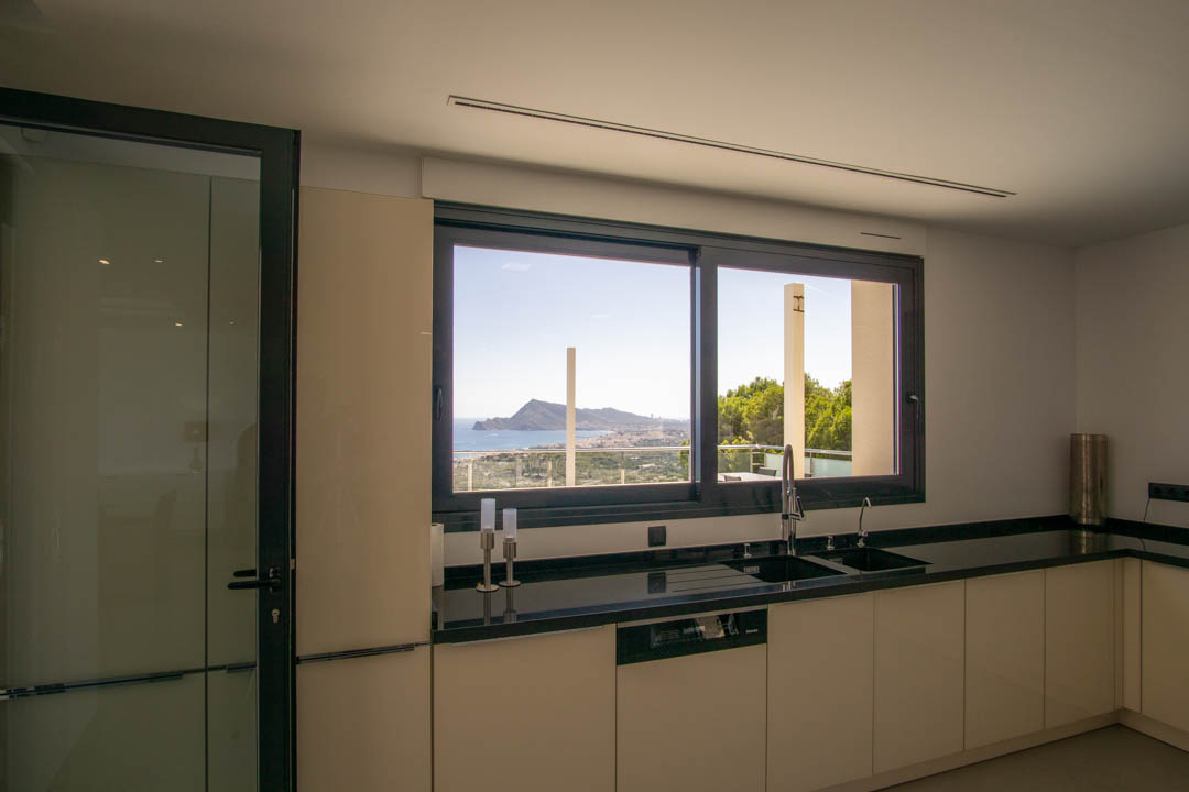 Moderne keuken met zwart granieten werkblad en geïntegreerde spoelbak. Een groot raam biedt direct uitzicht op de Middellandse Zee en de baai van Altea.