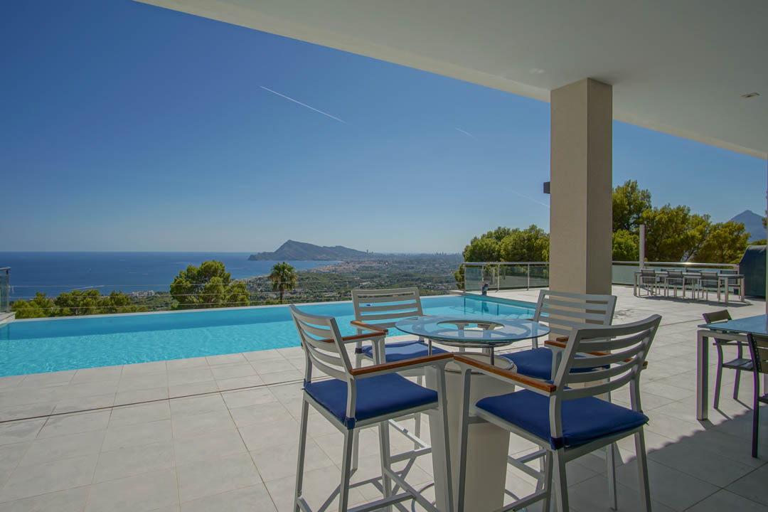 Ruim terras met overloopzwembad en panoramisch uitzicht op de baai van Altea. Voorzien van modern terrasmeubilair en lichte tegels.