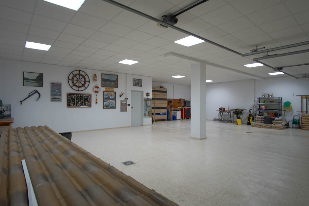Ruime garage voor vijf auto's met systeemplafond, LED-verlichting, een ingerichte werkplaats en wanden gedecoreerd met nautische elementen.