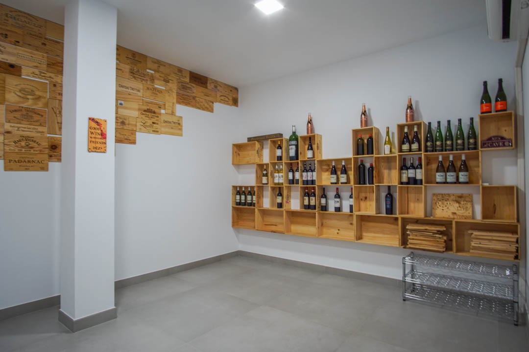 Wijnkelder met modulaire houten kistplanken en decoratieve wandpanelen, afgewerkt met een grijze tegelvloer en strakke witte muren.