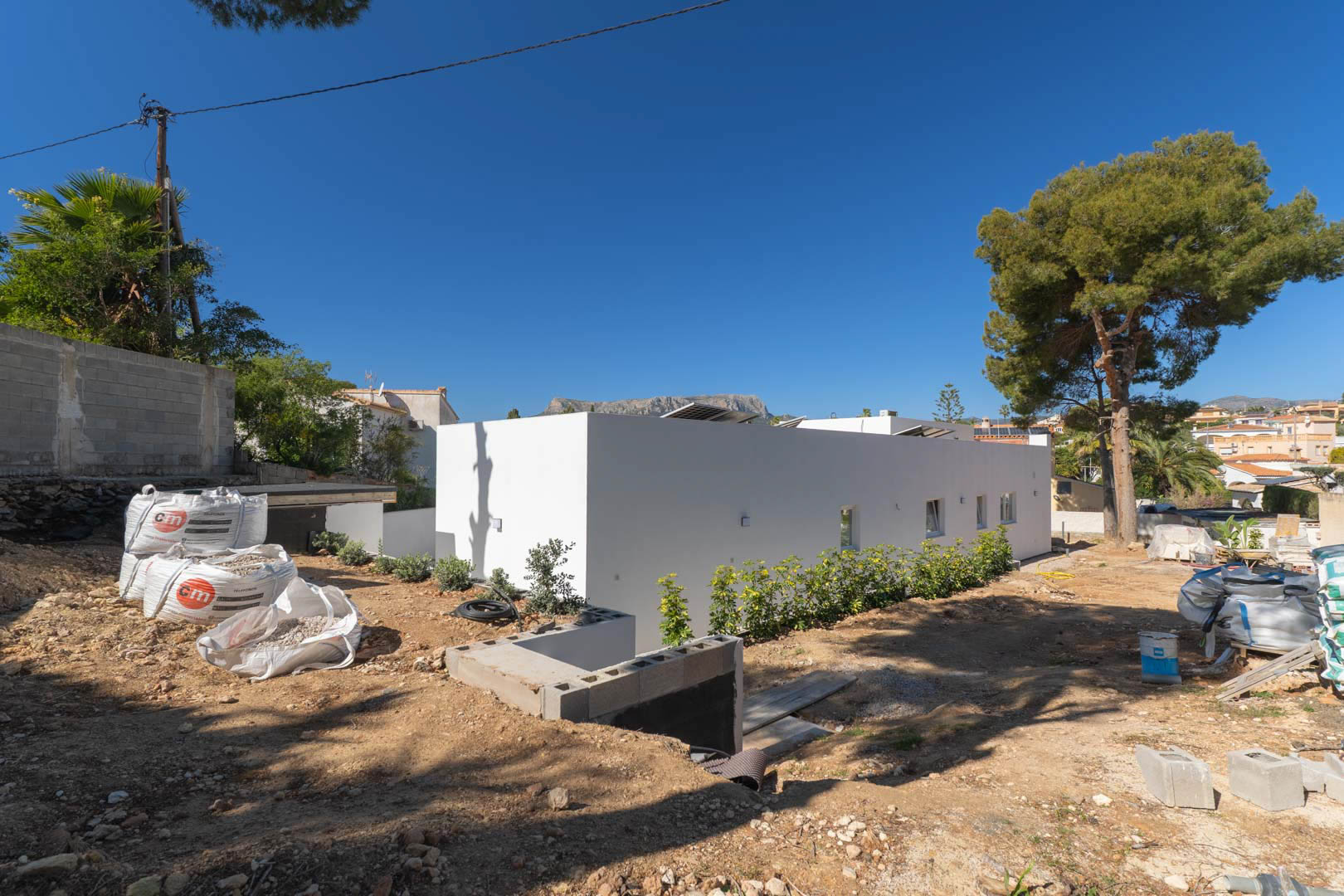Gelijkvloerse minimalistische villa met witte gevel en zonnepanelen op het dak. Het omliggende terrein bevindt zich momenteel in de fase van egalisatie en tuinaanleg.