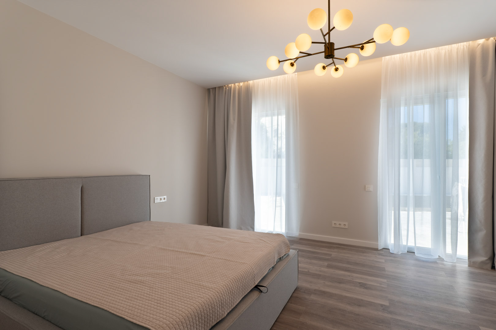 Minimalistische hoofdslaapkamer met grijze houten vloer, indirecte LED-verlichting en een eigentijdse moleculaire kroonluchter.