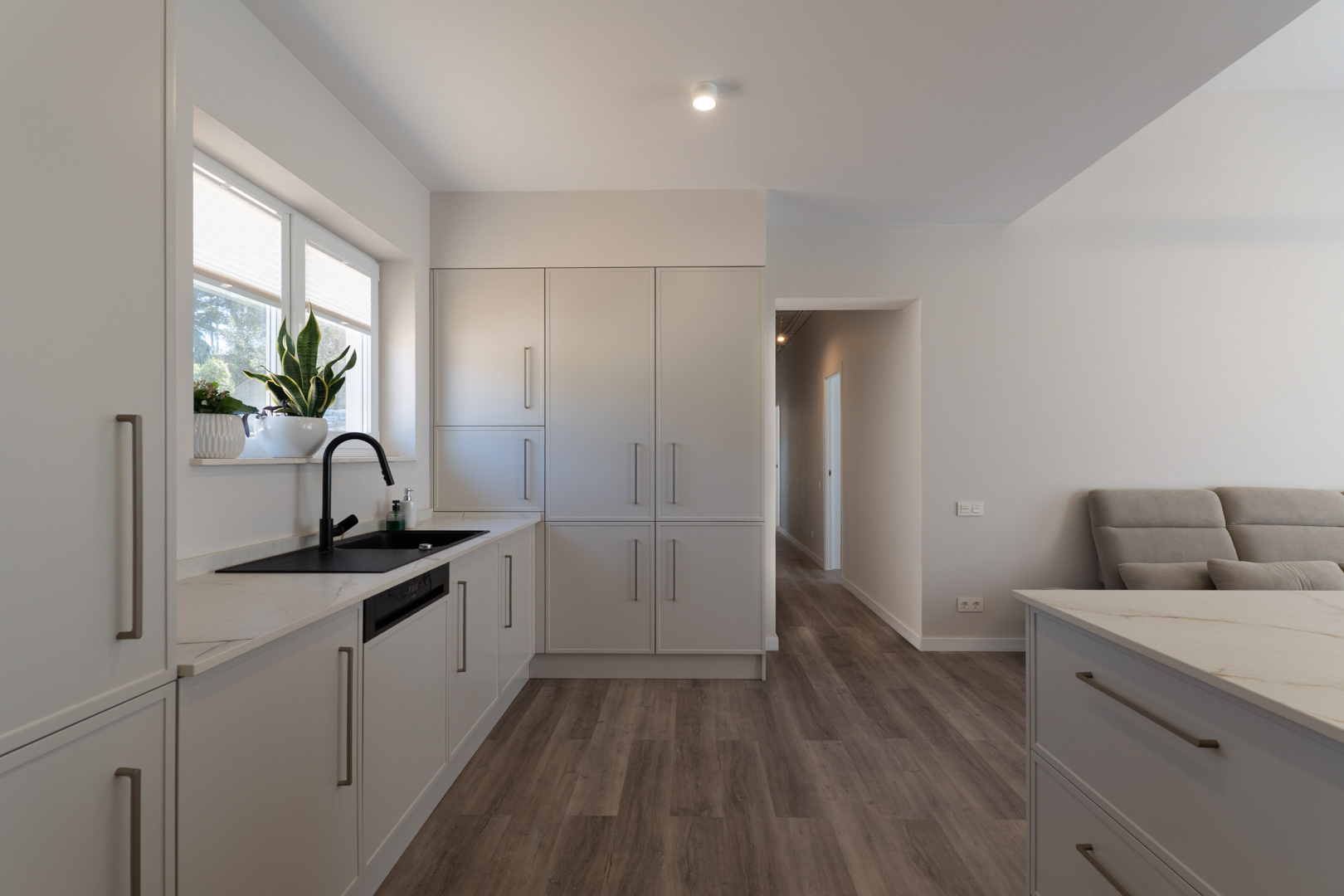 Minimalistische keuken met matwitte kasten, een stenen werkblad met aders en een zwarte kraan. De functionele indeling is voorzien van een houtlook vloer en natuurlijk licht.