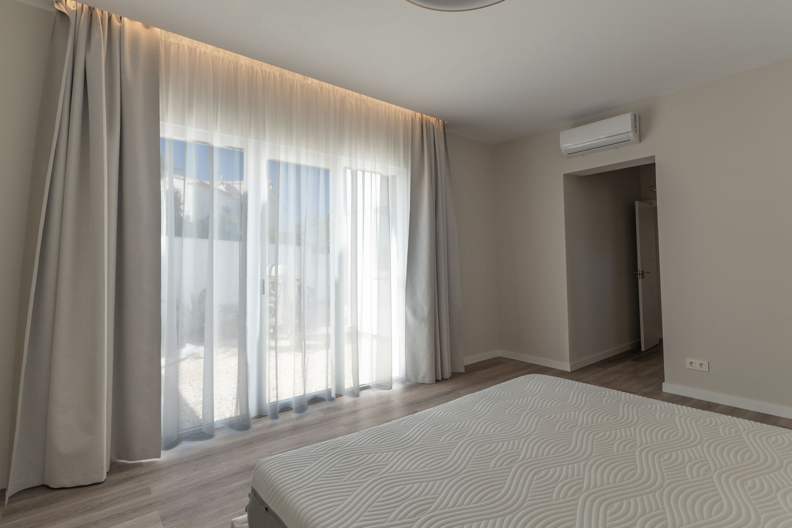 Minimalistische slaapkamer met grote glazen deuren, geïntegreerde LED-verlichting en airconditioning. Voorzien van een lichte houtlook vloer en directe toegang tot buiten.