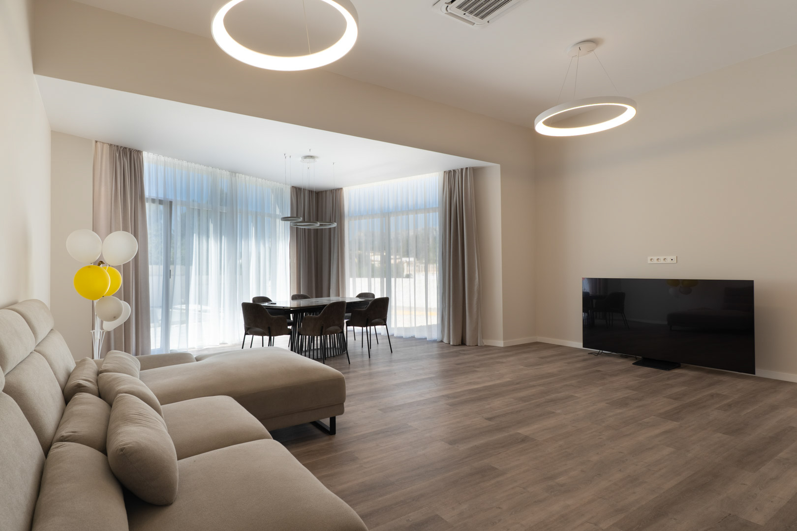 Open woon- en eetruimte met houtlook vloer, minimalistische ringverlichting en grote raampartijen die zorgen voor een lichte, moderne atmosfeer.
