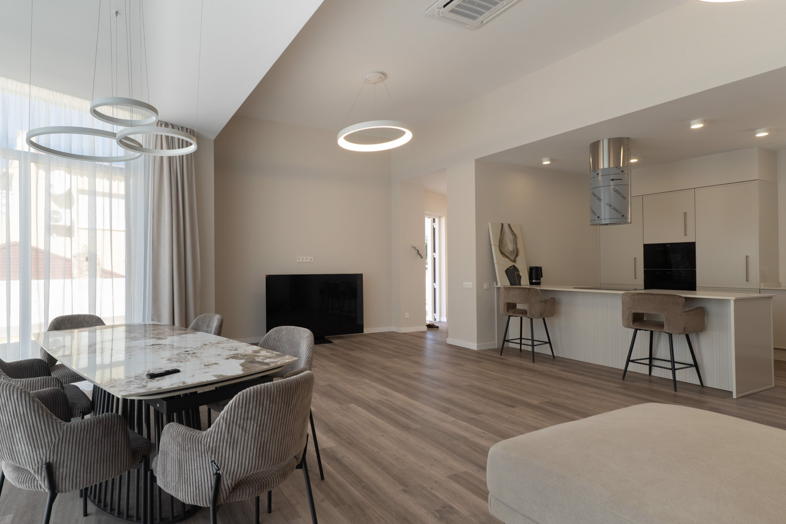 Open woonruimte met marmeren eettafel, minimalistische keuken met bar en moderne cirkelvormige LED-hanglampen op een warme houtlook vloer.