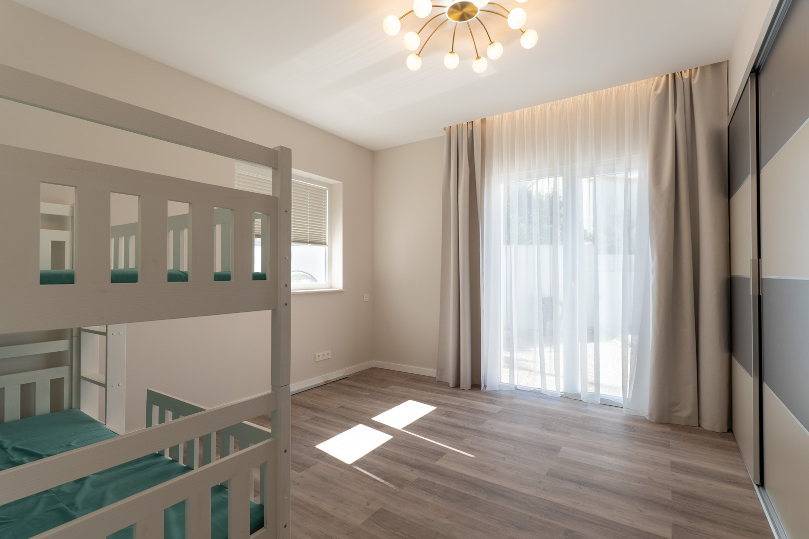 Slaapkamer met wit houten stapelbed, laminaatvloer en een ruime inbouwkast. Natuurlijk licht valt binnen via grote ramen met lichtdoorlatende gordijnen.