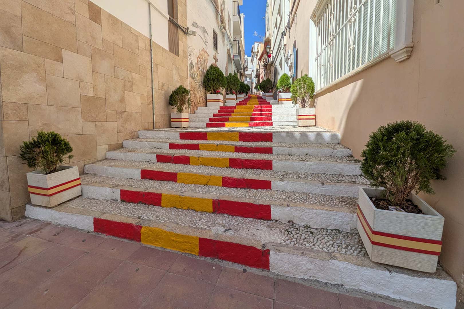 Voetgangersstraat in het oude centrum van Calpe met een stenen trap in de kleuren van de Spaanse vlag, omzoomd door plantenbakken en authentieke gevels.