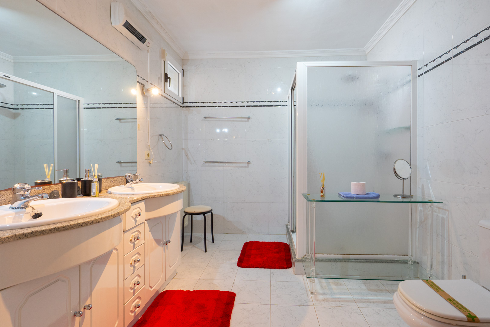 Badkamer met dubbele wastafel, granieten werkblad en witte kasten. Voorzien van een inloopdouche met matglas en individuele airconditioning.