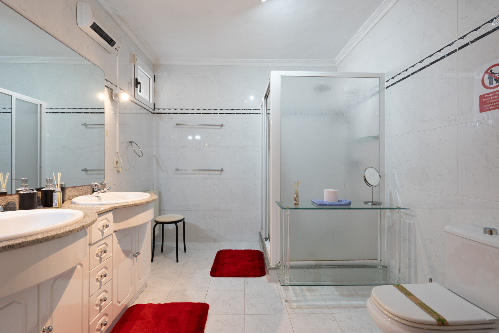 Badkamer met dubbele wastafel op een granieten blad, grote spiegel en douche met matglazen wand. Voorzien van split-airconditioning en volledig betegelde wanden.