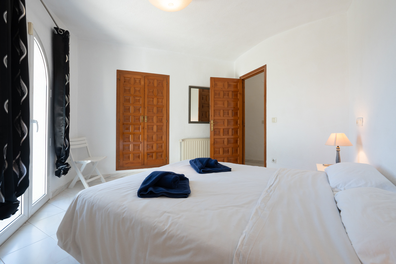 Lichte slaapkamer met traditionele houten inbouwkasten, een boogvormige glazen deur naar buiten en een lichte tegelvloer.