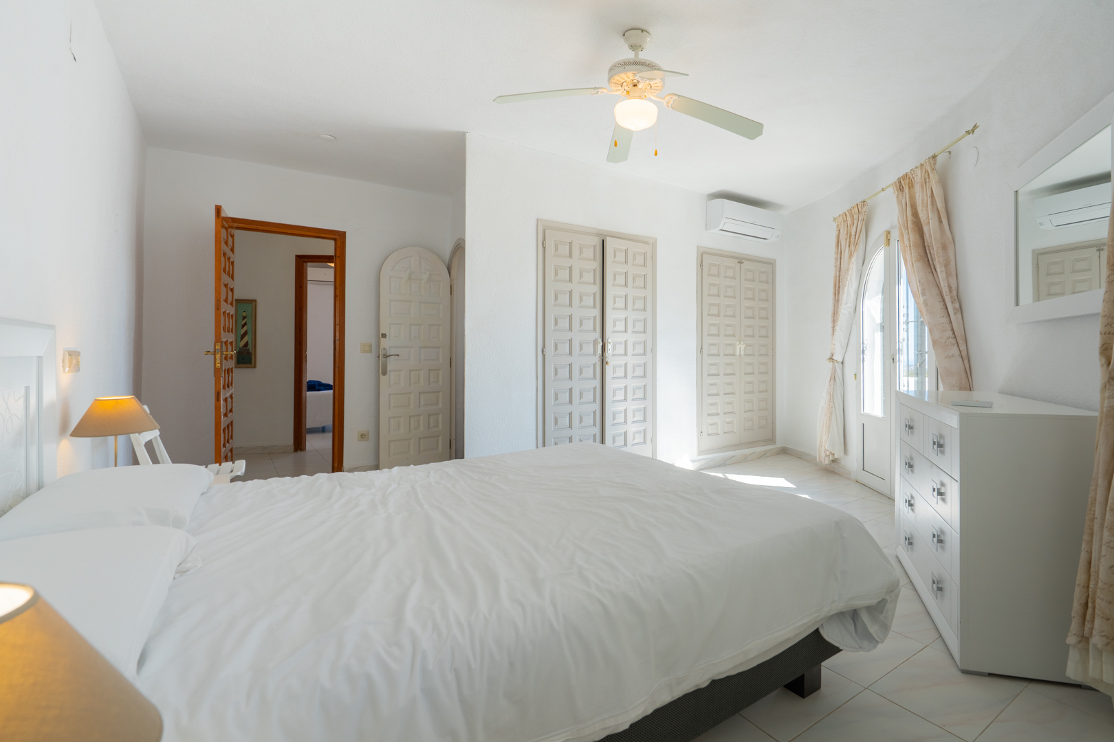 Lichte slaapkamer met traditionele inbouwkasten, airconditioning, een plafondventilator en directe toegang naar buiten via een glazen boogdeur.