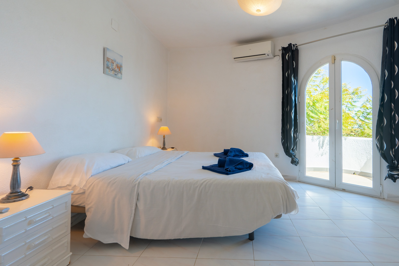 Lichtrijke slaapkamer met tweepersoonsbed, airconditioning en een boogvormige glazen deur met toegang tot het terras.