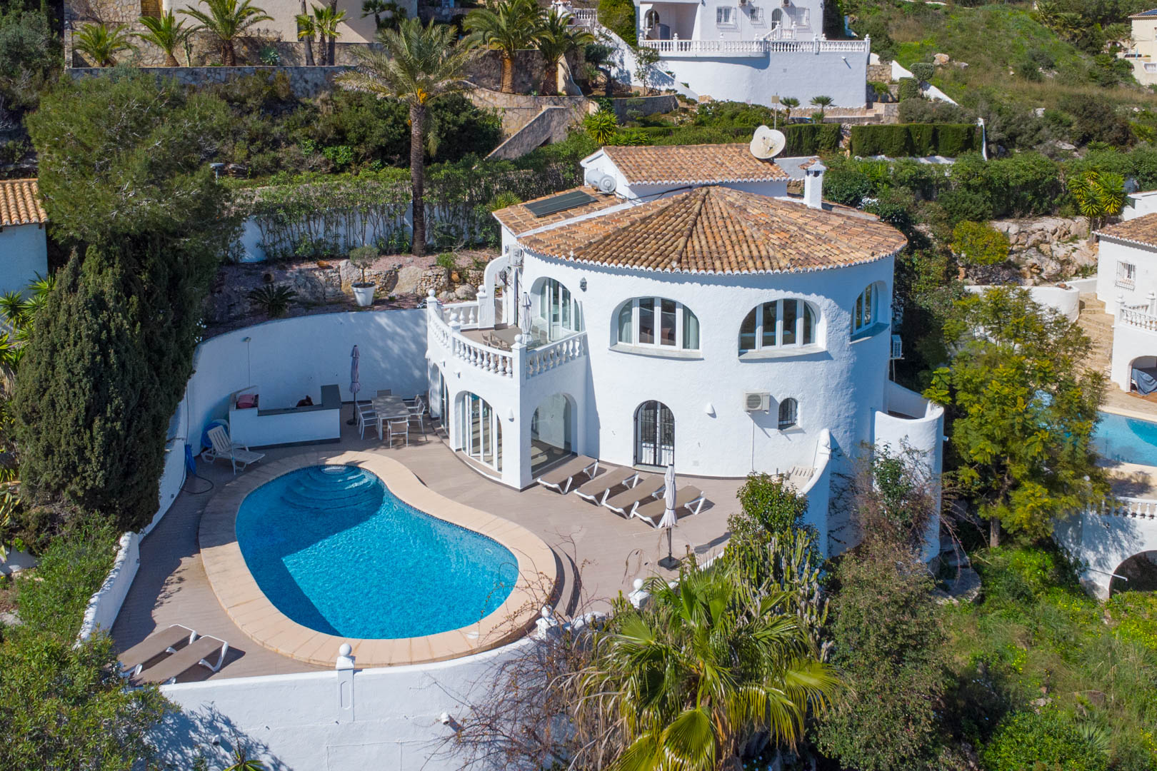 Luchtfoto van de villa met een niervormig zwembad, ruim zonneterras, traditionele witte gevel en zonnepanelen op het pannendak.