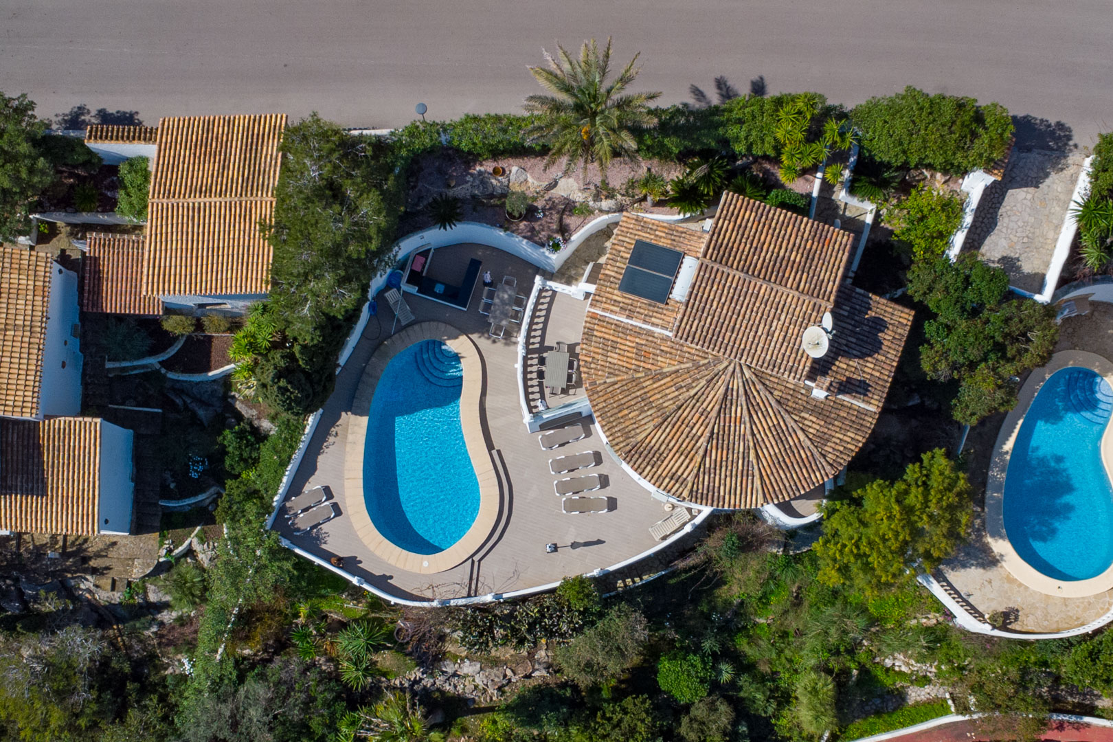 Luchtfoto van de villa met het niervormige zwembad, het riante zonneterras met buitenkeuken en het karakteristieke pannendak met zonnepanelen.