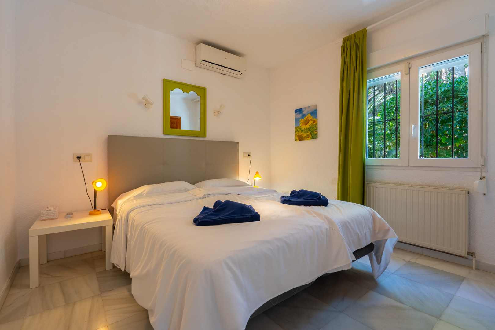 Slaapkamer met marmeren vloer, airconditioning en verwarming. Voorzien van een raam met beveiligingstralies, groene gordijnen en een bijpassende spiegel.