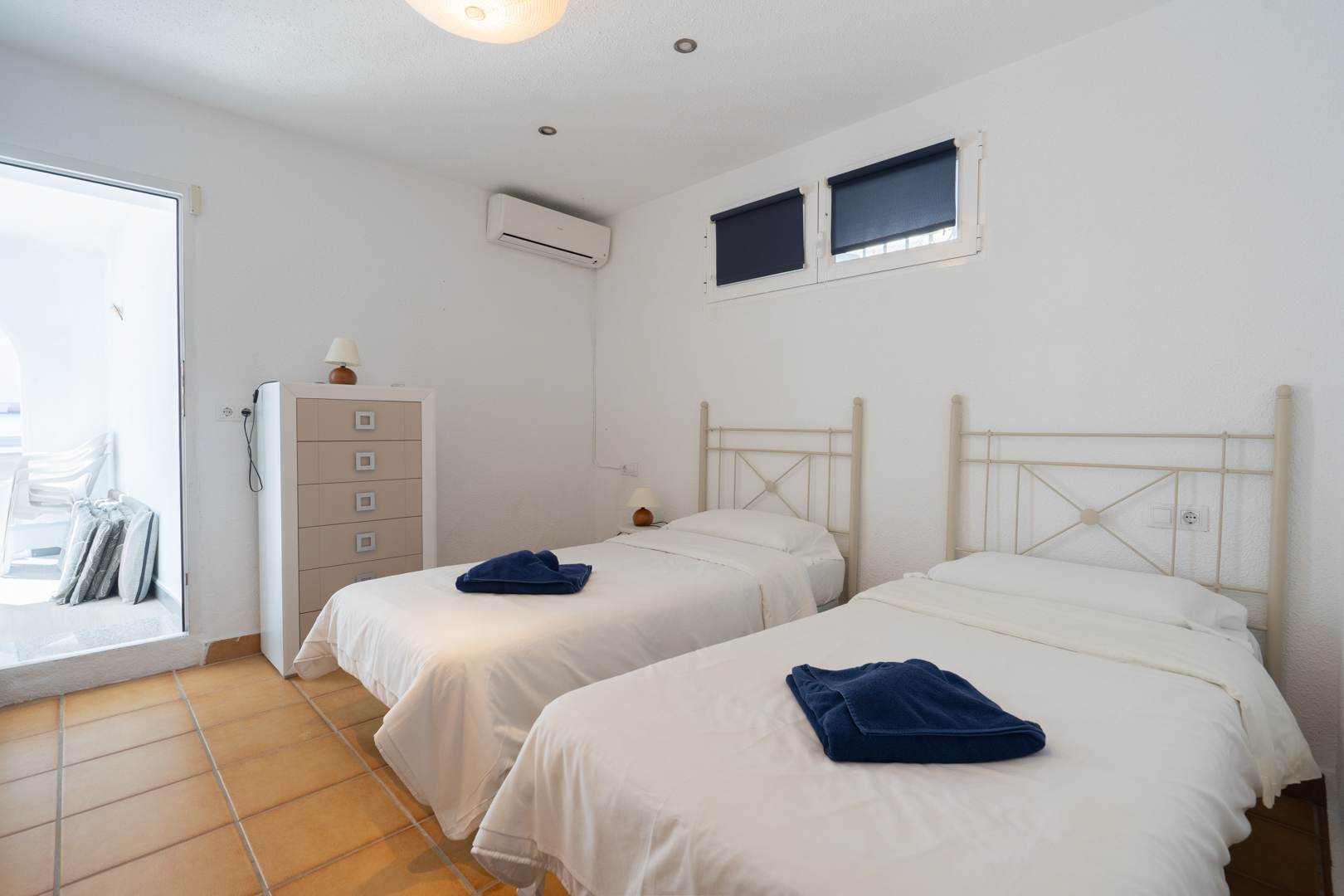 Slaapkamer met twee eenpersoonsbedden, terracotta tegelvloer en airconditioning. Inclusief directe toegang tot het terras en veel natuurlijk licht.
