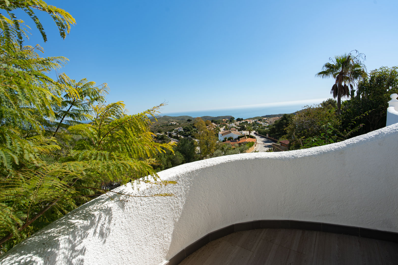 Terras met een gebogen witte structuurmuur en donkere vloertegels, met uitzicht over de Middellandse Zee en de groene omgeving van Cumbre del Sol.