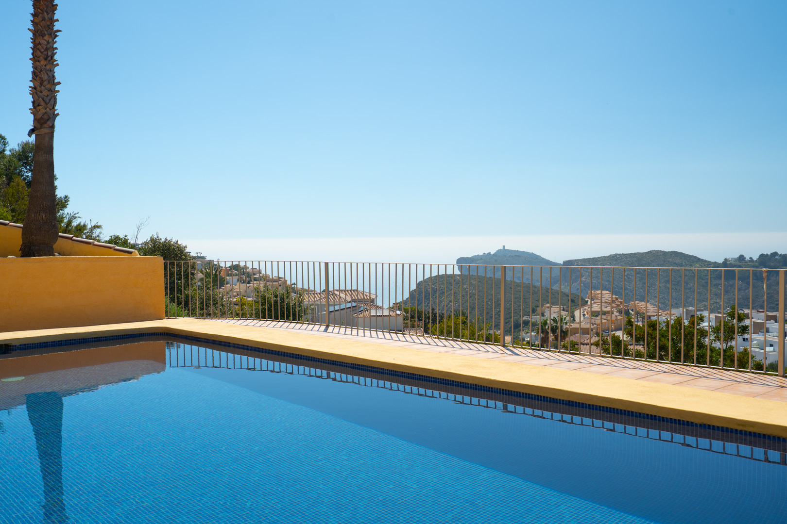 Blauw betegeld zwembad met panoramisch uitzicht op zee en de Cap d’Or in Moraira, grenzend aan een terras met metalen veiligheidsreling.