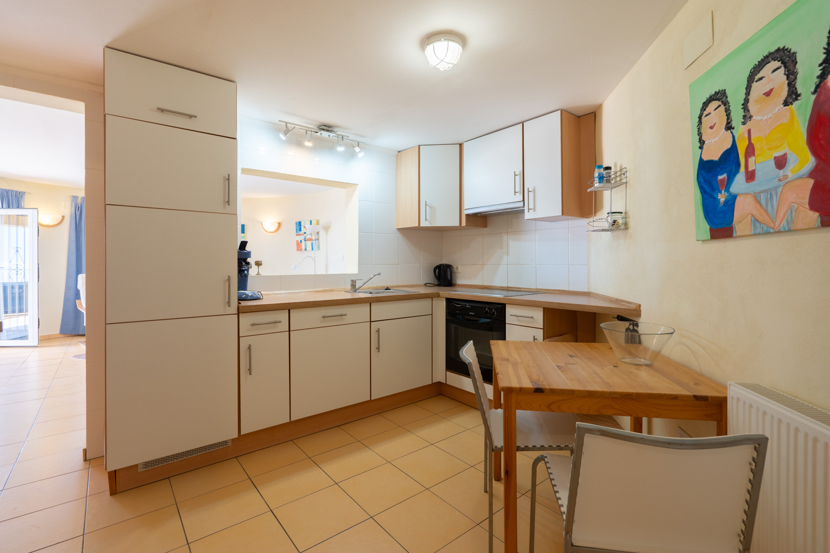 Functionele keuken met witte kasten, houten werkblad en een geïntegreerde eethoek. Voorzien van een doorgeefluik en een warme tegelvloer.