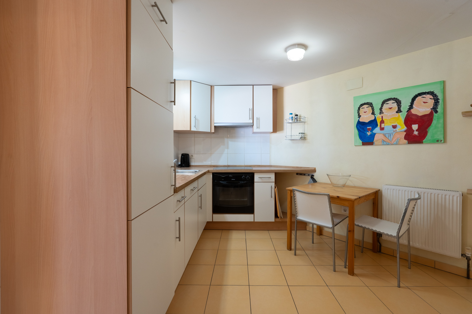 Functionele keuken van het gastenverblijf met witte kasten, houtlook werkbladen, een compacte eethoek en warmgekleurde keramische vloertegels.