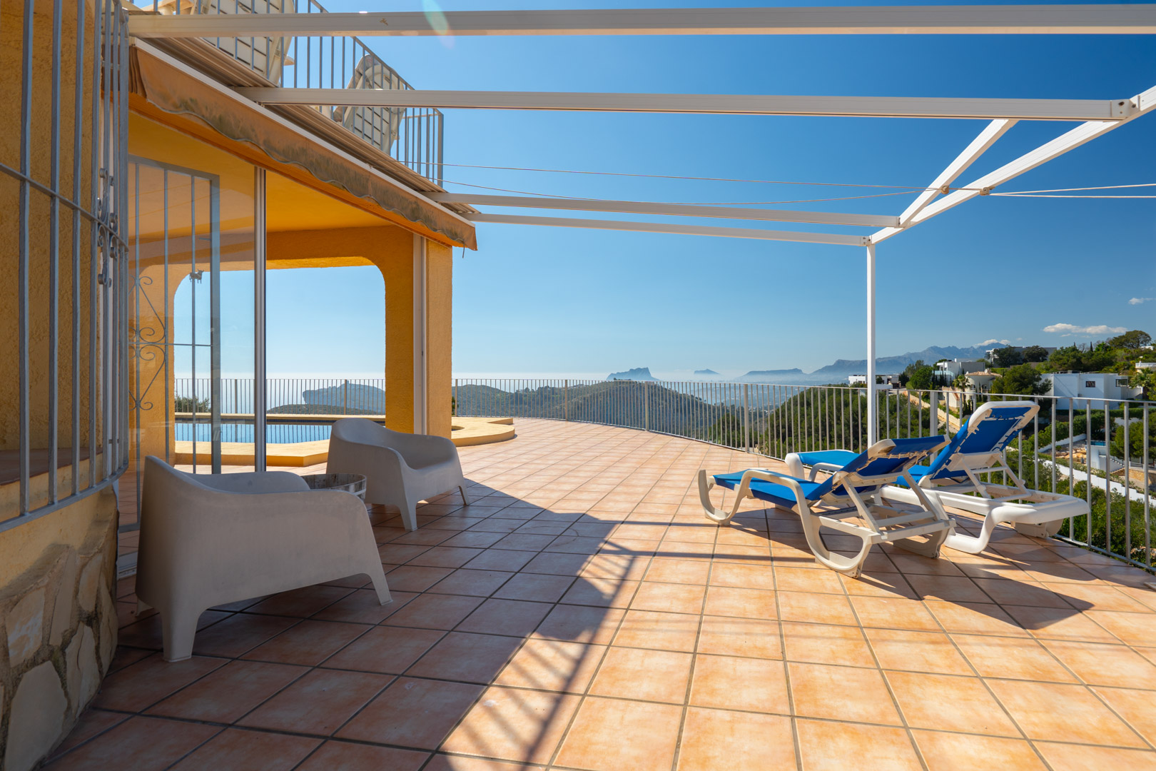 Groot zonneterras met terracotta tegels, metalen pergola en panoramisch uitzicht op de Middellandse Zee en het Bernia-gebergte.