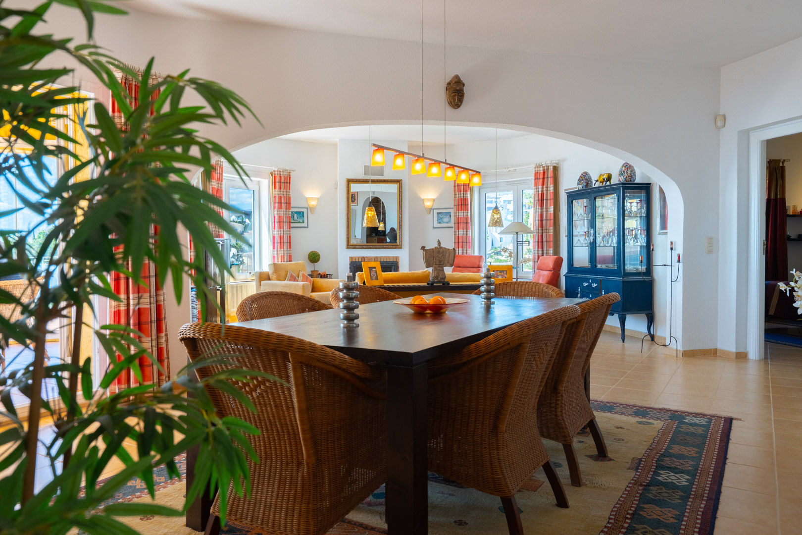 Lichte eetkamer met een donkerhouten tafel en rieten stoelen, verbonden met de woonkamer via een boog. Voorzien van een tegelvloer en natuurlijke lichtinval.