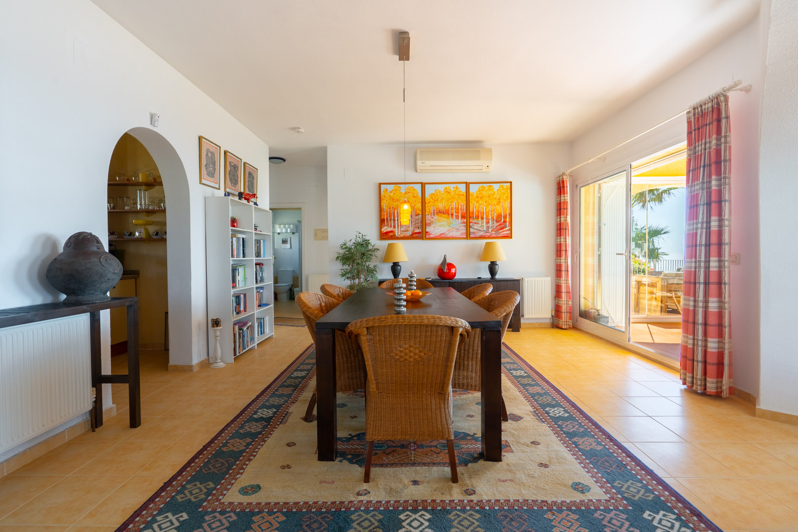 Lichte eetkamer met een donkerhouten tafel, rieten stoelen en directe toegang tot het terras via grote schuifdeuren. Voorzien van een traditionele boogdoorgang.