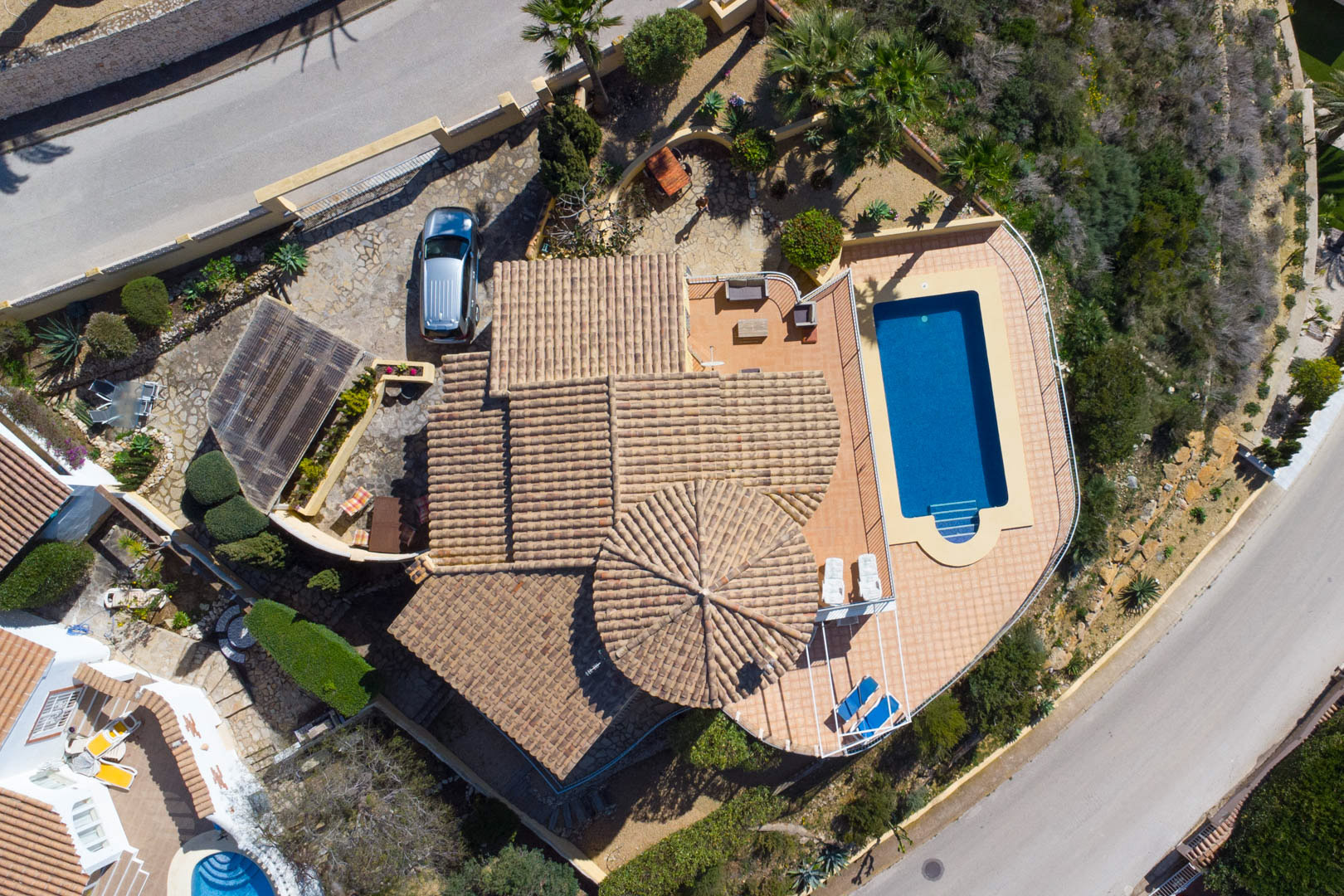 Luchtfoto van de villa met het traditionele pannendak, het rechthoekige zwembad met omliggend terras en de oprit met carport voor eigen parkeergelegenheid.